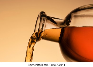 A Bottle Of Whiskey, Bourbon, Or Liqueur. Pouring Liquid, A Stream From The Neck. Close - Up Orange Background.