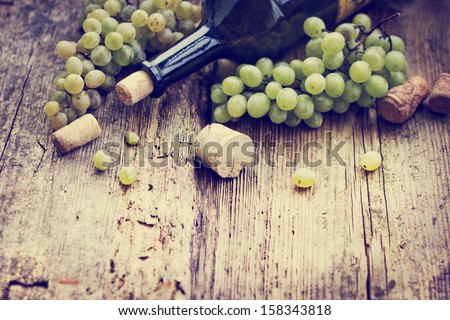 Bottle of white wine, grape and corks on wooden table