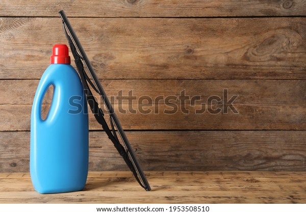 Bottle of windshield washer fluid and wiper on\
wooden table. Space for\
text
