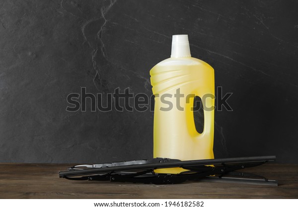 Bottle of windshield washer\
fluid and wipers on wooden table against black background. Space\
for text