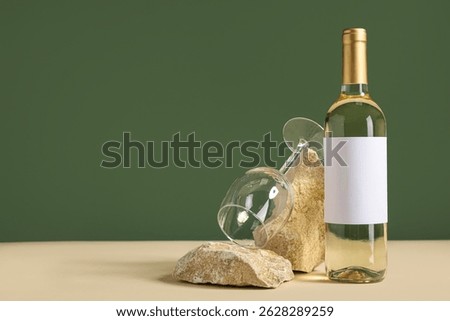 Bottle of wine with blank label, empty glass and stones on table against green background