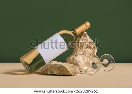 Bottle of wine with blank label, empty glass and stones on table against green background