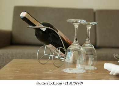 Bottle of wine and two empty glasses are on the table. Luxury hotel room service with wine bottle and two glasses. Cozy romantic atmosphere.