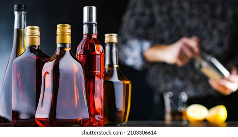 Bottles of assorted alcoholic beverages and a bartender preparing a drink with a cocktail shaker