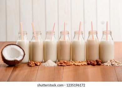Bottles of assorted vegan milk and different ingredients on wooden table. Organic dairy-free drinks to replace cow's milk.