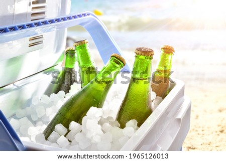 Bottles of beer chilled on ice in a camping fridge on a beach on a hot day with sunshine.