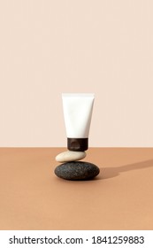 Bottles of cosmetic cream with balancing stones on beige background in sunlight. Minimal style cosmetics template