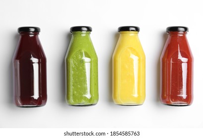 Bottles with delicious colorful juices on white background, flat lay