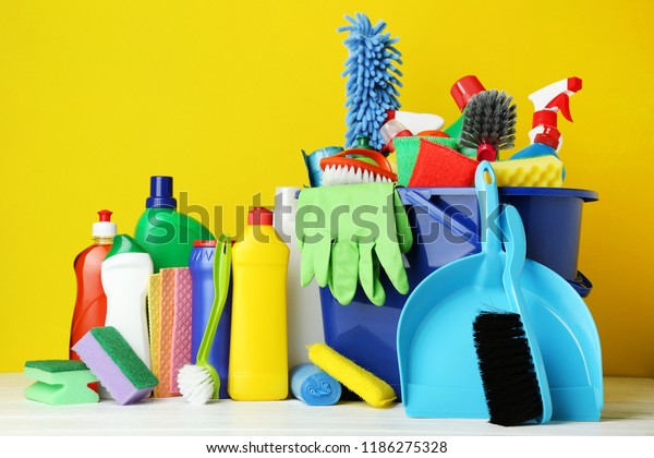 Bottles with detergent and cleaning tools on\
yellow background