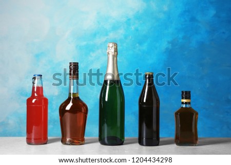 Bottles with different alcoholic drinks on table against color background