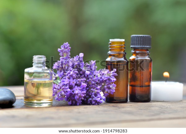 bottles of essential oil among lavender flower\
arranged on a wooden table in garden\
