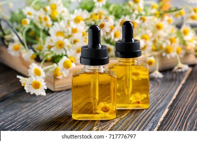 Flaschen mit ätherischem Öl und Kamillenblumen auf Holztisch