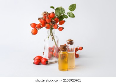 Bottles of essential oil and rose hip berries isolated on white background