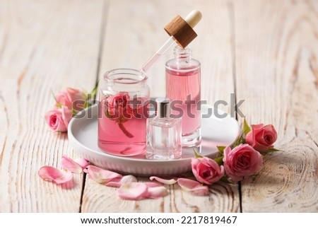 Bottles of essential rose oil and flowers on white wooden table
