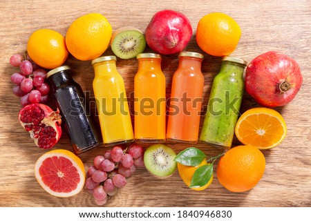 bottles of fruit juice with fresh fruits on a wooden table, top view