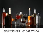 Bottles and glasses with different alcoholic drinks on table against gray background
