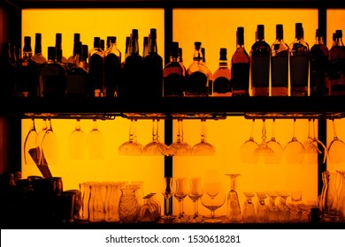 Bottles and glasses sitting on shelf in a bar, back lit, brand names removed