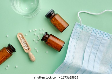 Bottles of homeopathic granules, water glass for preparation of medicinal solution, protective medical mask. View from above.