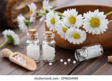 Bottles of homeopathy granules. Homeopathic remedy - Chamomilla. Daisies flowers in wooden bowl. Homeopathy medicine concept. 
