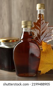 Bottles And Jar Of Tasty Maple Syrup On Wooden Table