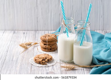 Bottles of milk with blue straws and chocolate chip cookies on wooden background - Powered by Shutterstock