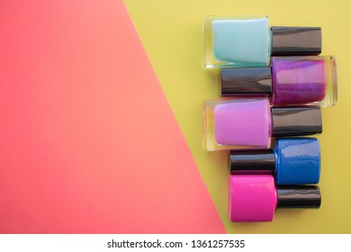 Bottles of nail polish. A group of bright manicures on a pink, yellow background. With empty space on the left. View from above