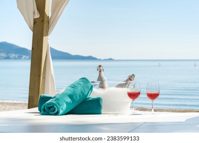 Bottles and pair of wineglasses with cold rose wine placed with rolled beach towels on canopy bed for romantic evening on seashore - Powered by Shutterstock - Get 15% off with code: PIKWIZARD15