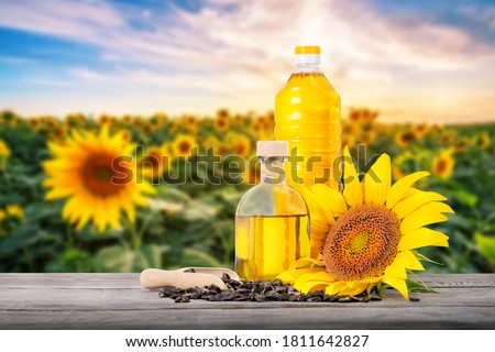 Bottles of sunflower oil with seeds and flower on a wooden table against the background of a field with sunflowers