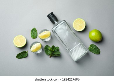 Bottles of vodka, shots, lime slices and mint on gray background