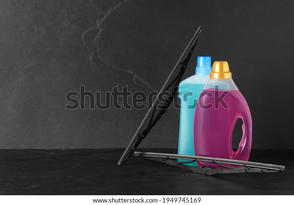 Bottles of windshield washer fluids and wipers on\
black table. Space for\
text