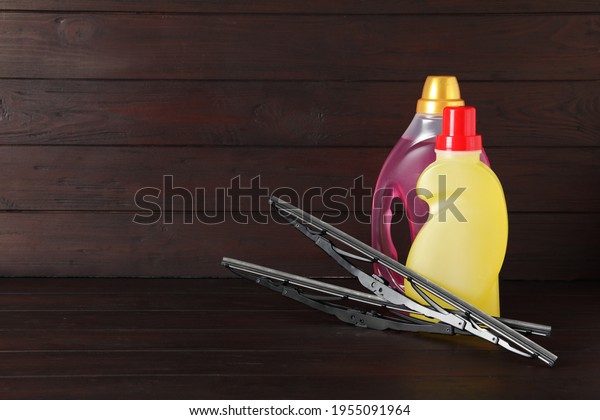 Bottles of windshield washer fluids and wipers on\
wooden table. Space for\
text