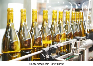 bottles with wine on bottling and sealing conveyer production  line at modern winery factory. Shallow DOF.