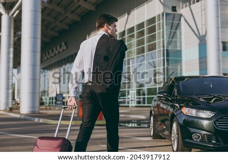 Bottom back side view young traveler businessman young man wearing black dinner suit walk go outside at international airport terminal with suitcase to car book taxi Air flight business trip concept.