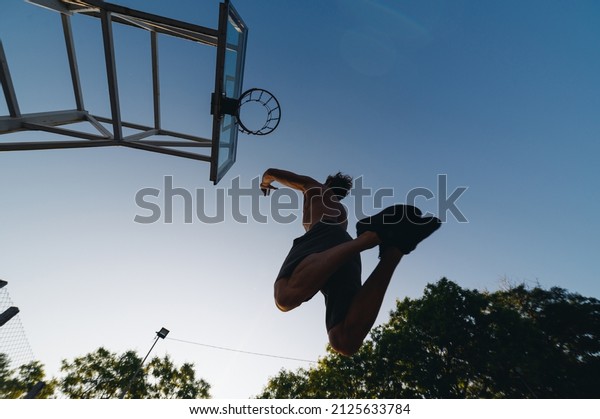 Bottom back view young strong sportsman man with\
naked torso shoot free throw jump scoring basket training ball at\
basketball game playground court on sky background Outdoor\
courtyard sports concept