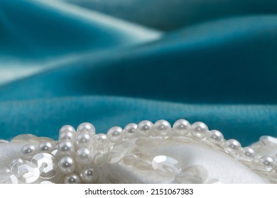 A Bottom Border Of Beaded Ivory White Satin Wedding Dress Trim Decorated With Faux Pearls And Sequins, With A Wavy Turquoise Fabric Background.