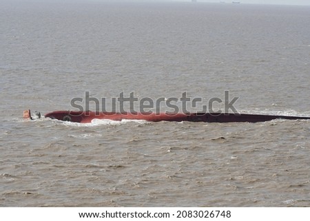 Bottom of capsized ship painted red brown with visible rudder and propeller in strong current of the muddy dirty southern estuary of the Yangtze River in the approach to the Shanghai, China.