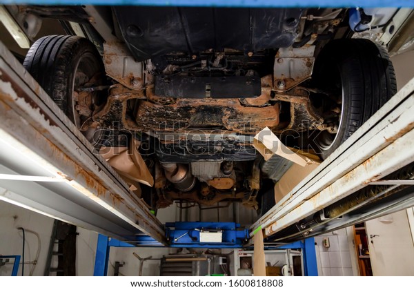 The bottom of the car lifted on a lift covered\
with brown and orange rust during anti-corrosion treatment. Auto\
service industry.