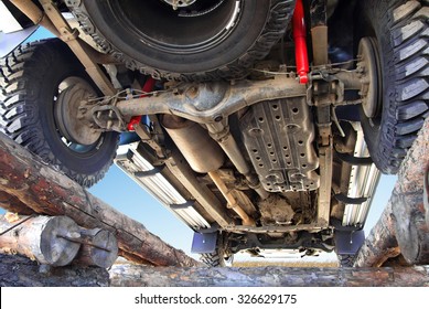 The bottom of the jeep, car bottom, off-road vehicle, car on the country road, a prestigious transport, horizontal image, jeep standing on the logs, inspection jeep below, car against the sky.