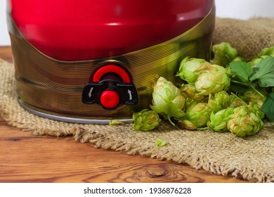 Bottom Part Of The Red Disposable Mini Keg Of Beer With A Built-in Beer Tap Among The Hop Cones On Sackcloth On Rustic Table Close-up
