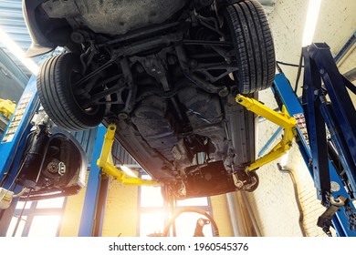 Bottom POV big modern SUV car with removed gearbox raised on lift elevator at workshop service maintenance station center. Vehicle check-up and repair. Underbody chassis and suspension parts