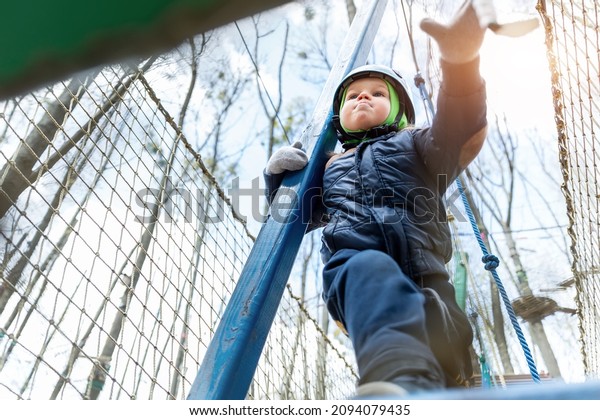 Bottom POV view brave courage little toddler child
boy wear safety equipment helmet enjoy passing obstacle course
forest rope adventure park on cold winter day. Active outside
leisure amusement camp