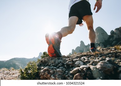 Bottom of running sneaker shoe sole on hard rocky terrain on mountain path during ultra trail marathon race. Strong fit healthy athletic man, trained legs during workout outdoors - Shutterstock ID 1034321524