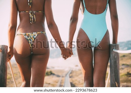 Bottom of two beautiful young women walking holding hands in a wooden foot bridge at the beach