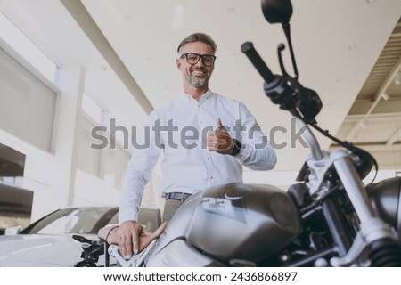 Bottom view adult man customer male buyer client wear shirt show thumb up choose bike to buy new black motorbike or automobile in car showroom vehicle salon dealership store motor show Sales concept