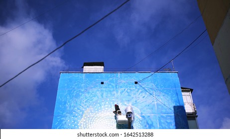 Bottom view of an artist using elevating crane for drawing breathtaking graffiti on blue cloudy sky background, time lapse effect. Art. Street art concept, man with a spray paint.