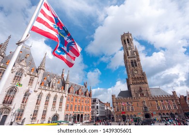Bottom view of the Belfort Tower and the flagpole with the flag of Bruges from the side of the square in Bruges against the backdrop of a beautiful sky with white clouds, Belgium