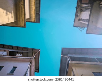 bottom up view between 4 old buildings with a clear blue sky in the background.  These buildings have white or cream-colored walls with some parts that appear weathered, such as water stains and moss 