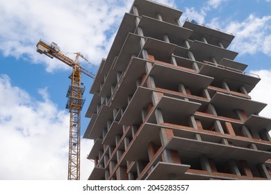 Bottom view of a building under construction. Tower crane on top and  blue sky.