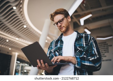 Bottom view of caucasian guy watching something on laptop computer in office space. Concept of flexible workplace. Idea of freelance and remote work. Young focused bearded successful man in glasses - Shutterstock ID 2122768712