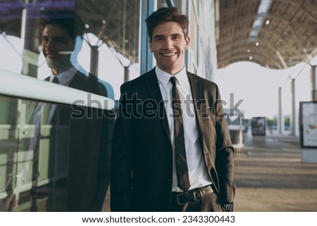 Bottom view cheerful young traveler brunet businessman man in black classic tie suit standing outside at international airport terminal look camera. People air flight business trip lifestyle concept